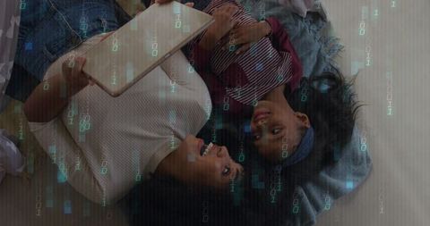 Overhead view of mother and daughter sharing tablet on bed with binary code overlay
