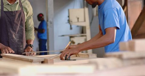 Coworkers measuring wooden plank in carpentry workshop