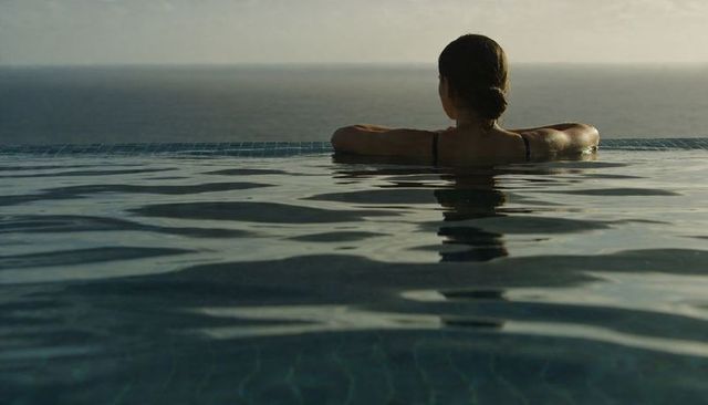 Woman resting in infinity pool overlooking ocean horizon during tranquil sunset moment