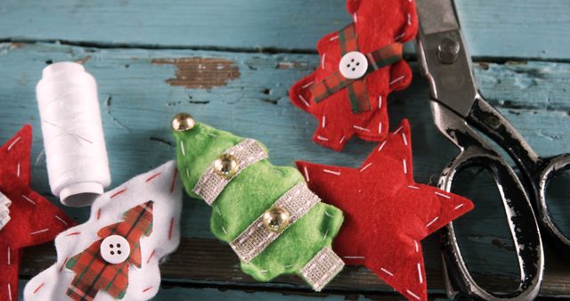 This scene displays handmade Christmas ornaments fashioned from felt, with a focus on a rustic wooden backdrop and holiday themes such as a Christmas tree and stars. Crafting supplies like scissors and thread illustrate an inviting DIY project in progress. Perfect for blogs or websites focused on holiday crafts, interior holiday design, or sustainable holiday decorating tips.