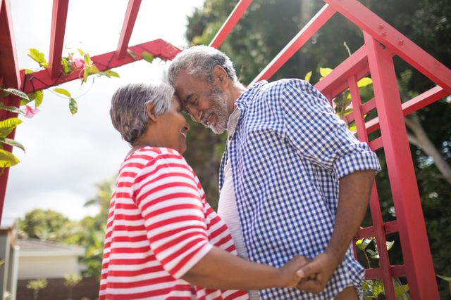 Low angle view of affectionate senior couple standing by metallic structure in yard