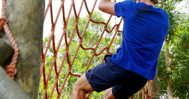 A man demonstrates determination by climbing a rope net in an outdoor fitness course. - Download Free Stock Photos Pikwizard.com