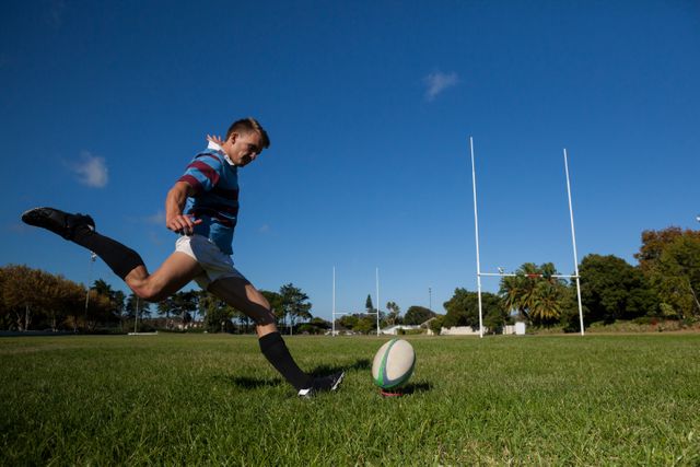 Rugby player in action kicking ball towards goalposts on a sunny day. Ideal for use in sports-related content, fitness and training materials, team-building promotions, and outdoor activity advertisements.