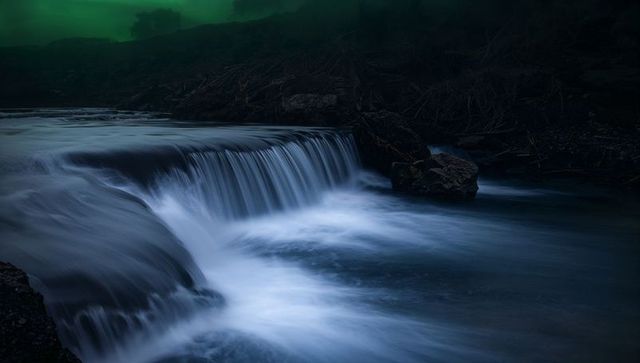 Flowing silky waterfall curtain at dusk with driftwood and mossy boulders, long exposure