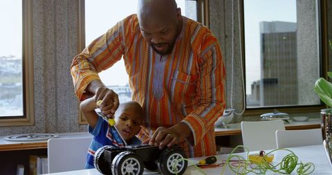 Father Guiding Young Son in Toy Car Repair at Home