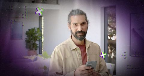 Indian man holding smartphone in modern home interior with plants and glass door, bearded