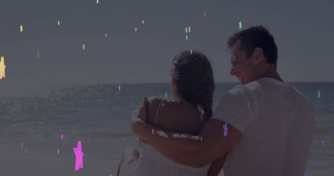 Couple on beach enjoying tranquil sunset with stars overlay