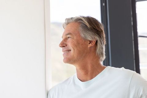 Mature man gazing through window in bright modern apartment, relaxed lifestyle