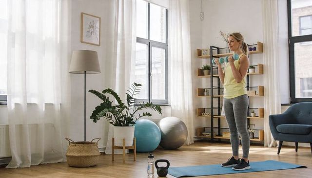 Woman performing bicep curls with turquoise dumbbells in sunlit living room
