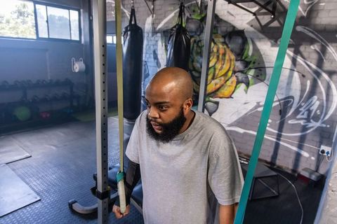 Bearded man standing at squat rack using suspension straps in urban gym with mural