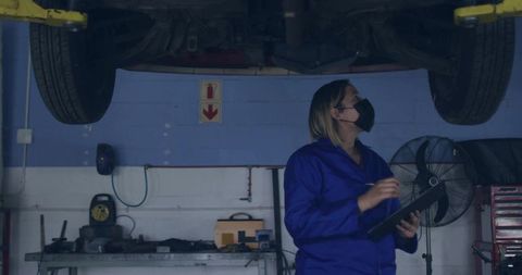 Auto Mechanic in Blue Overall Examining Car in Repair Garage