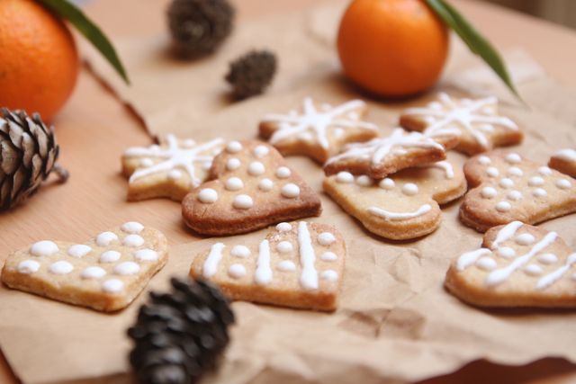 Decorative Christmas gingerbread cookies with icing and snowflake details on wooden table surrounded by pinecones and oranges, adding a festive holiday feel. Perfect for use in holiday recipes, seasonal blog posts, Christmas greeting cards, or festive promotional materials.