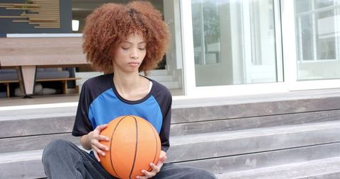 African american woman sitting on steps holding basketball, casual athletic lifestyle