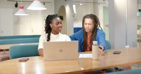 African American colleagues collaborating at coworking table reviewing charts on laptop