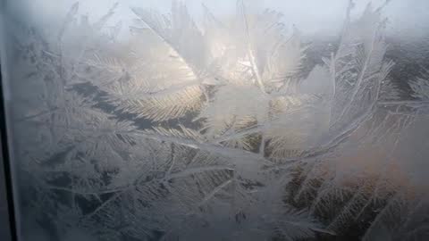 Panning across frost-covered window revealing intricate ice crystals in soft backlight