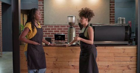 Two baristas discussing orders behind wooden coffee bar in cozy brick cafe