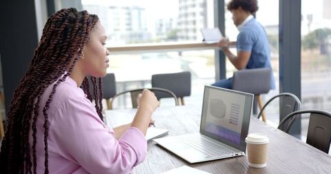 Businesswoman Taking Notes and Working on Laptop in Modern Office