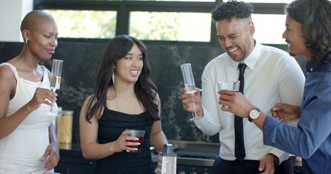 Diverse adults toasting with champagne and cocktails in semiformal home kitchen celebration