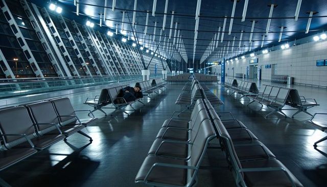 Sleeping traveler lying across seats in empty late-night airport terminal with backpack