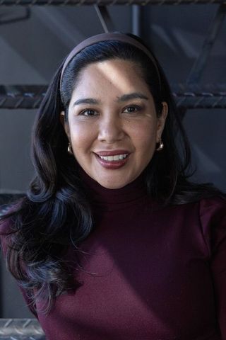 Smiling woman wearing burgundy turtleneck, gold hoops and headband on metal stairs