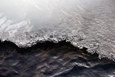 Crystal ice edge melting into dark flowing river water with ripples and reflections