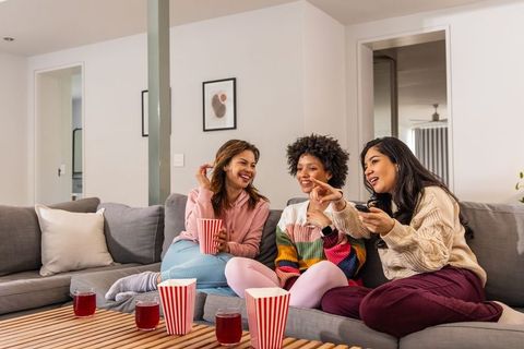 Multicultural friends enjoying cozy movie night on gray sectional sofa with popcorn