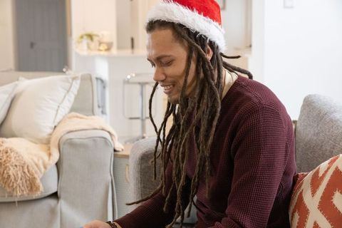 African american man wearing santa hat relaxing on couch at home during holidays