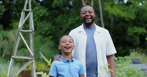 African american father and son laughing together in backyard garden with wooden trellis