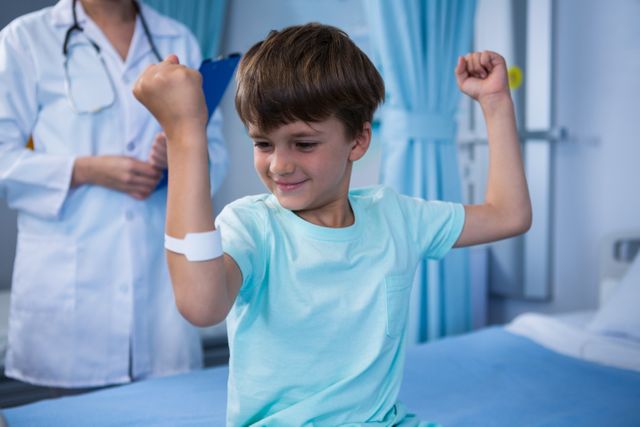 Boy flexing his muscles and female doctor standing in background in ward