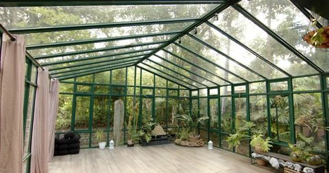 Sunlit green metal-framed conservatory with pitched glass roof and indoor tropical plants