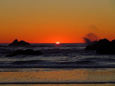Sunset over pacific ocean with silhouetted sea stacks and waves splashing shoreline