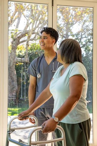 Caregiver Assisting Senior With Walker Near Glass Door