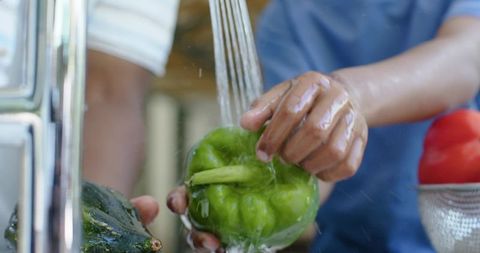 African american father and son washing green bell pepper under faucet at kitchen sink