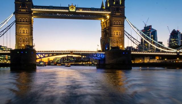 Tower bridge glowing at dusk with river thames reflections and illuminated london skyline