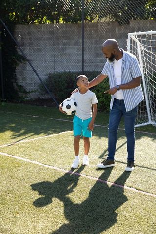 Father teaching son soccer basics on sunny turf field