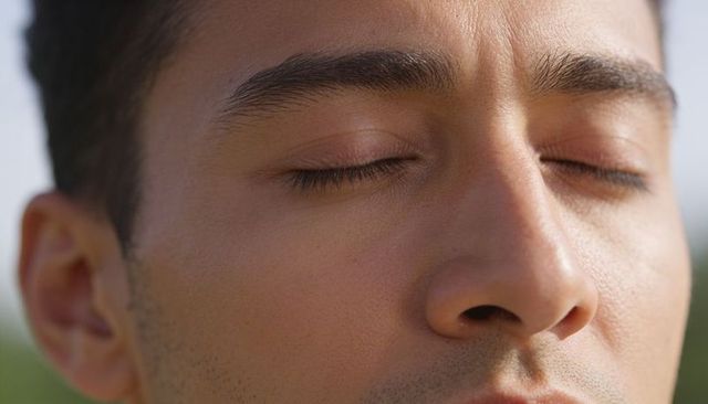 Young man closing eyes soaking sunlight closeup serene face with stubble and long lashes