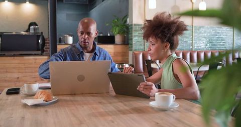 African american colleagues collaborating with laptop and tablet in urban coffeehouse
