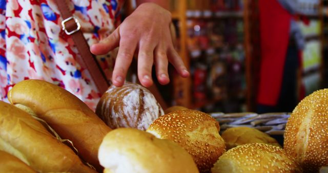 Hand reaching for bread at market stall with variety of baked goods. Ideal for use in advertising bakery products, illustrating food markets, or accompanying articles on artisan bread.