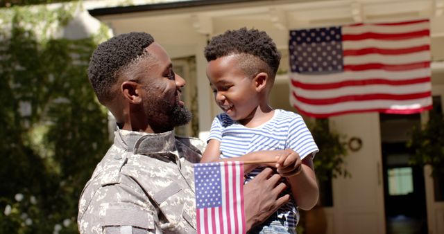 Happy african american son with flag welcoming home soldier father. Military service, returning home, celebration, patriotism, childhood, fatherhood and family, unaltered
