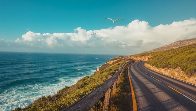 Coastal scenic highway curving along cliff with ocean waves and seagulls at golden light