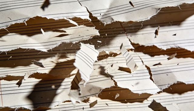 Torn Sheet Music Strips Scattered on Tabletop Showing Staff Lines and Frayed Edges Closeup
