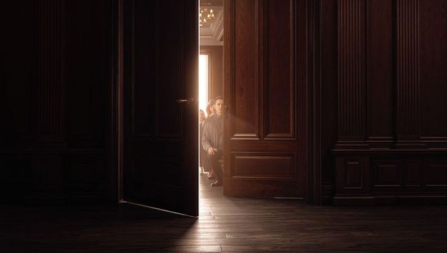 Sitting man peeking through ornate wooden door into sunlit room backlit silhouette