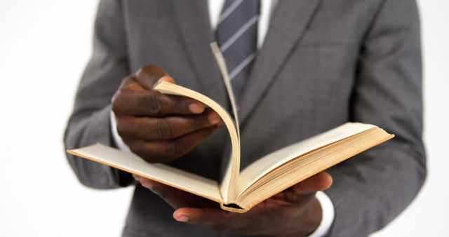 An African American businessman in a suit is browsing through a book, with copy space. His focus on the content suggests he's searching for information or preparing for a meeting.