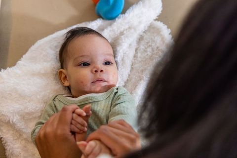 Infant bonding with caregiver holding hands on fluffy blanket in cozy gentle nursery moment
