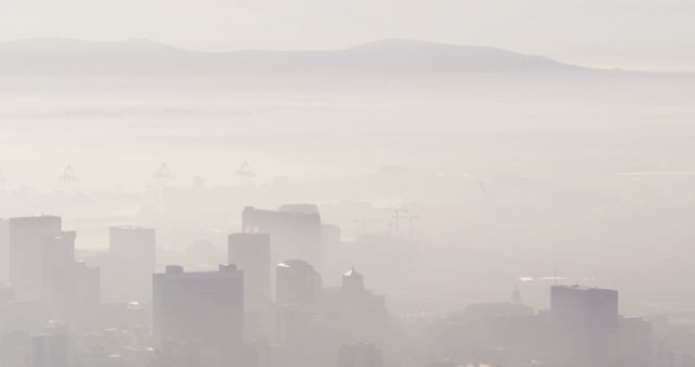 This image capturing a hazy city skyline enveloped in heavy fog, with mountains faintly visible in the background, can be perfect for showcasing urban pollution issues, environmental articles, or illustrating the effects of weather in city environments. Ideal for use in climate change publications, atmospheric studies, and urban development projects.