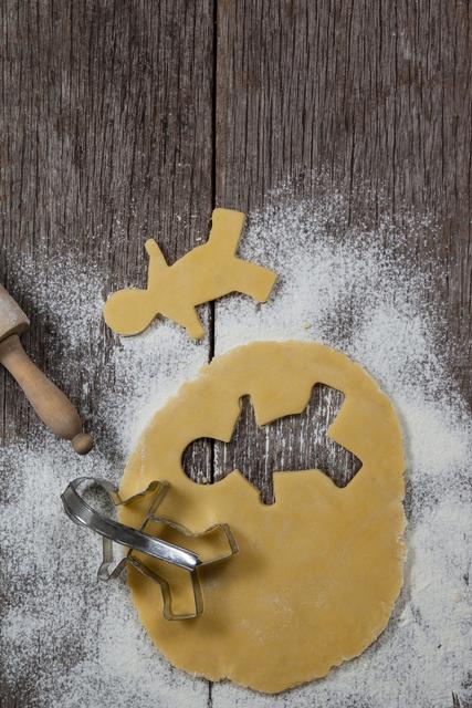 Dough with gingerbread shape and cookie cutter on a plank