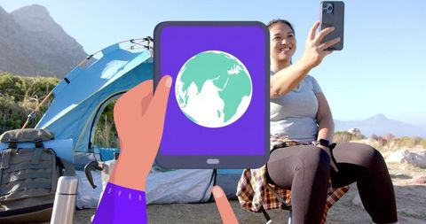 Smiling woman taking selfie at mountain camp with tablet showing globe and camping gear