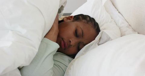 Mid-adult african american woman sleeping peacefully under white duvet in minimalist decor