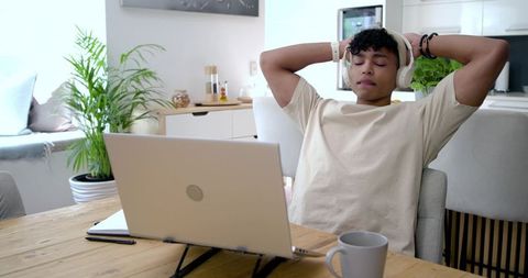 Young African American man relaxing with headphones at sunlit modern home workspace