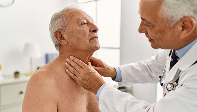 Doctor examining senior male patient neck and throat during routine medical checkup in clinic